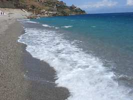 Brevi attimi delle onde del mare che si infrangono sulla spiaggia, composta da ghiaia, di colore blu-turchese.