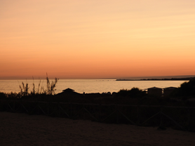 Panorama verso il mare durante il tramonto, con il cielo colorato da dolci sfumature di arancione riflesse dal mare tranquillo.